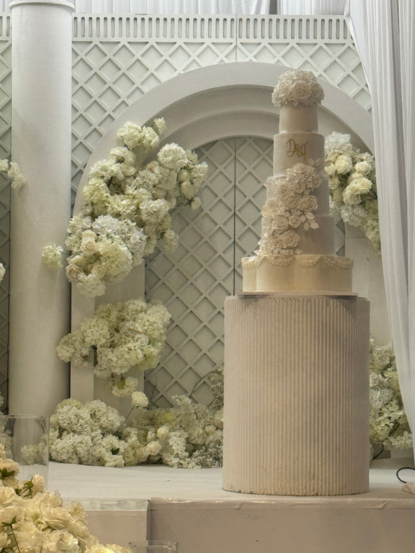 A tiered floral wedding cake styled against a cream lattice backdrop
