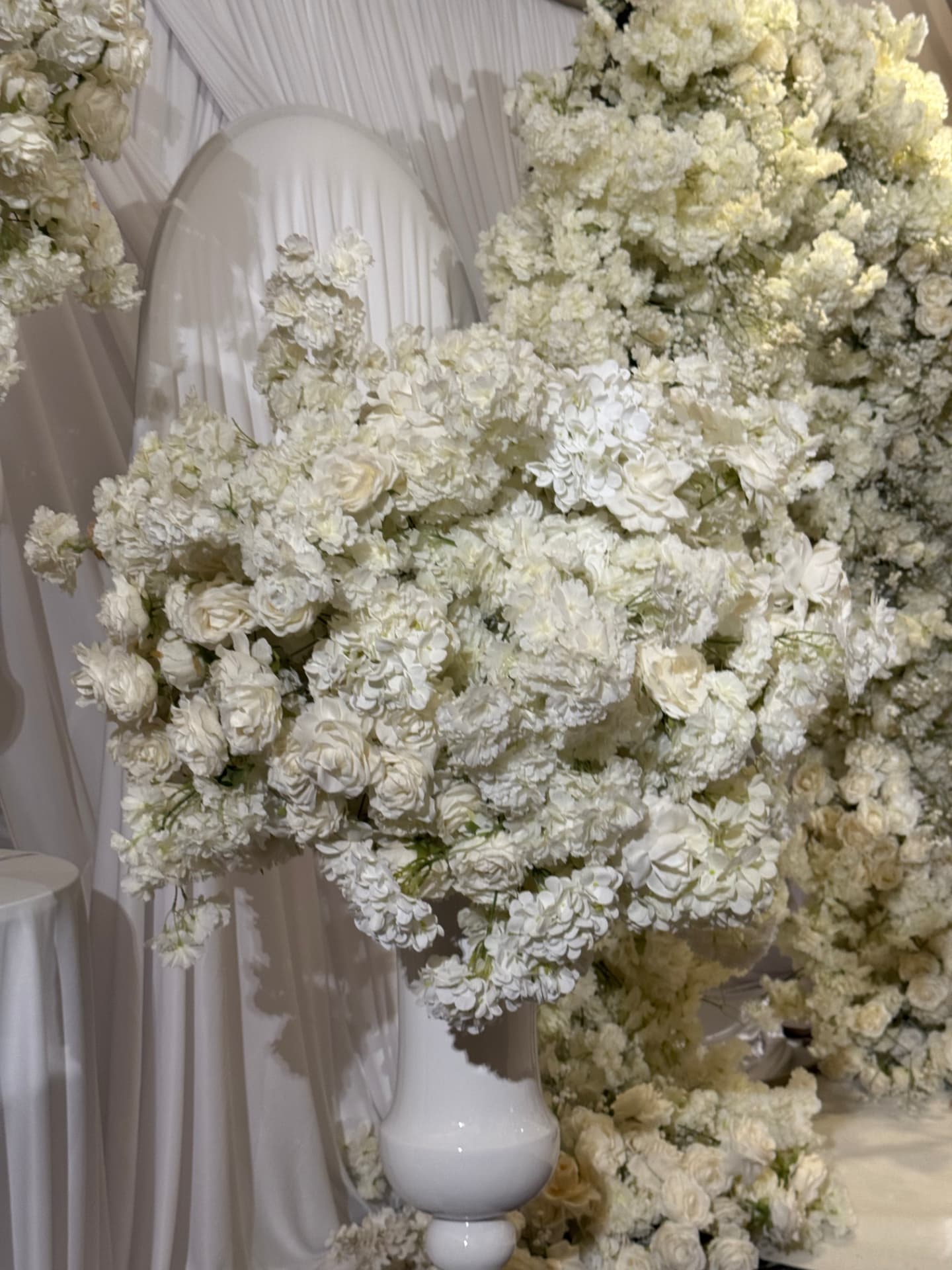 A wall of white florals and draped fabric dressing the wedding venue