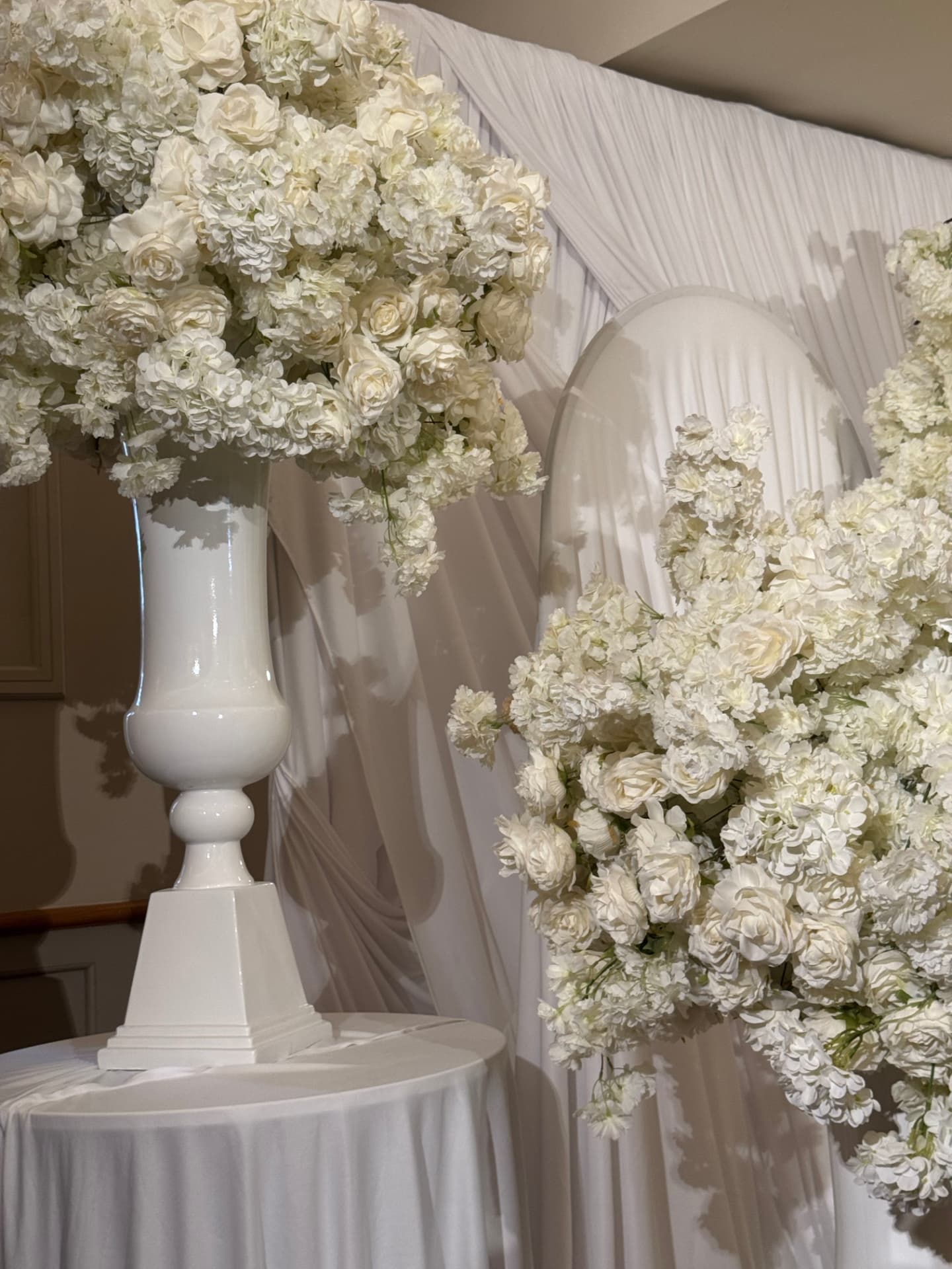 White floral arrangements in ceramic urns against soft draped fabric
